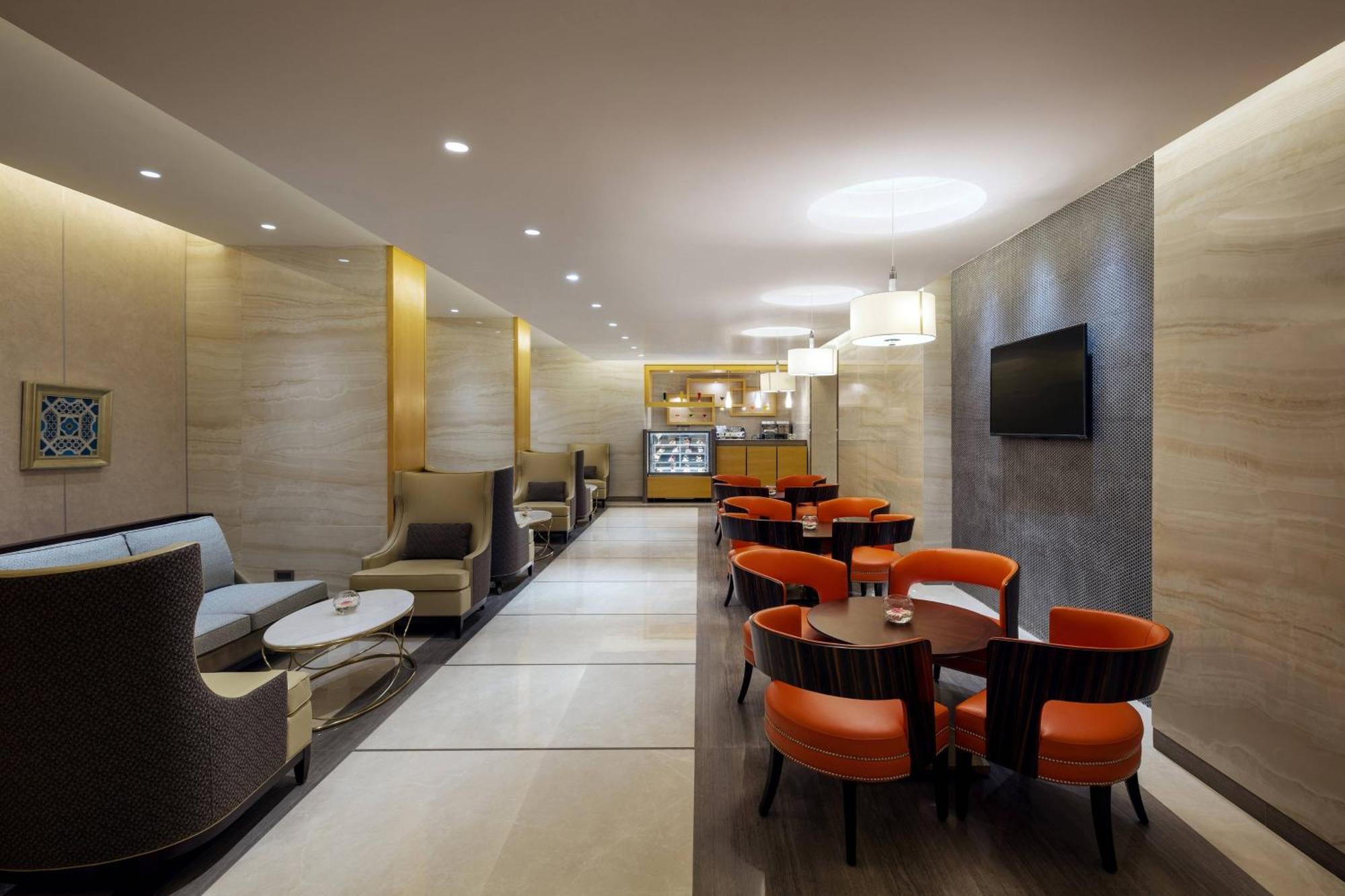 فندق شيراتون مكة جبل الكعبة المظهر الخارجي الصورة The photo depicts a modern and elegant lounge or café area. The interior features soft, warm lighting and a combination of neutral and bold color schemes. On the left side, there are comfortable seating arrangements with light-colored sofas and chair
